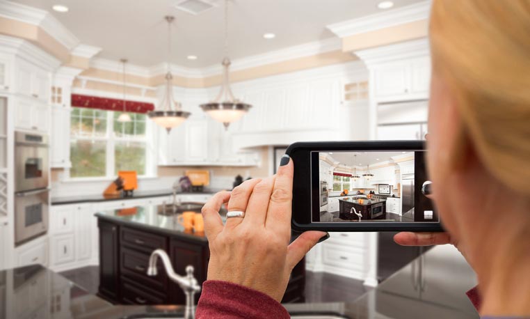 Third person perspective of woman taking photo of kitchen with her smartphone in landscape mode