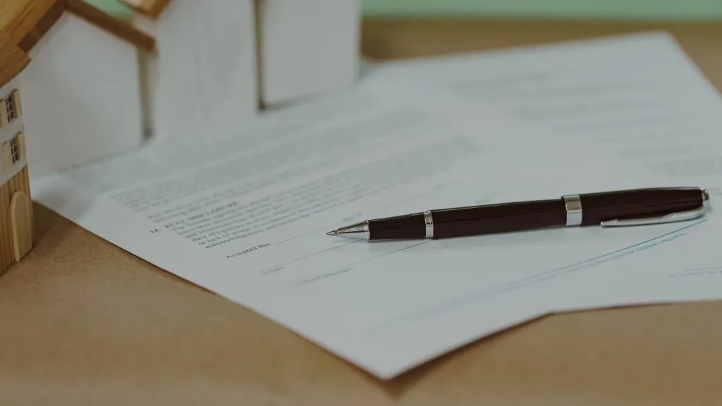 Real estate contract with pen and miniature houses on wooden desk